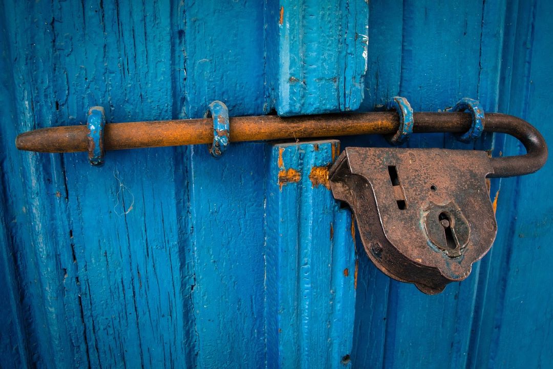 Porte bleue en bois, abimée et avec un cadenas rouillé.