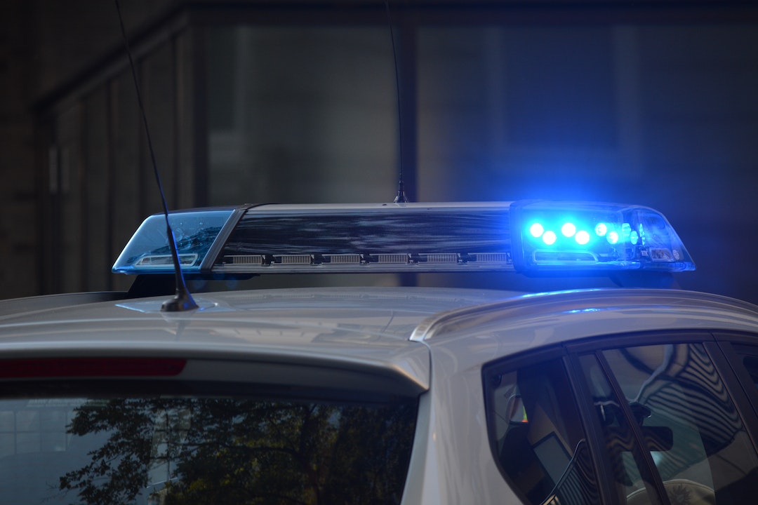 Voiture de police blanche avec un gyrophare bleu allumé.